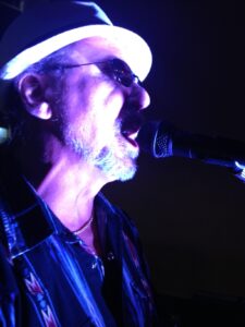A musician passionately singing into a microphone, illuminated by colorful stage lights.